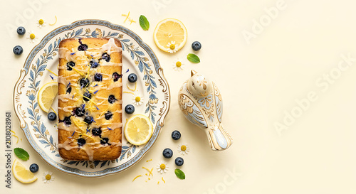 Flat lay featuring a vegan blueberry lemon loaf cake on a vintage plate with a handcrafted ceramic bird on a warm cream background..