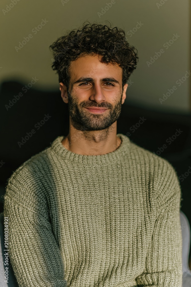 Fototapeta premium Smiling man with curly hair and knit sweater indoor portrait for lifestyle headshot and social media profile
