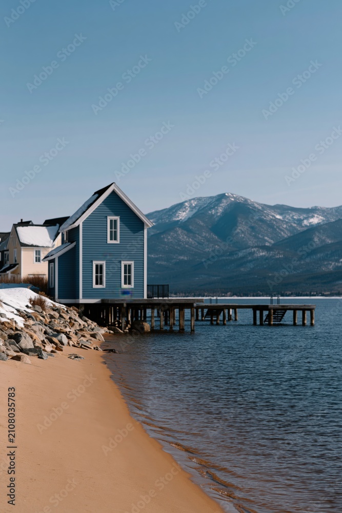 Fototapeta premium Blue lakeside house on stilts by a sandy beach with mountain view for waterfront wallpaper and background design