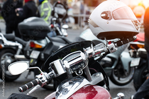 Obraz na plátně Modern motorcycle with white helmet on handlebars, covered in raindrops, parked outdoors during day, chrome details reflecting light, street scene with other vehicles and blurred people background