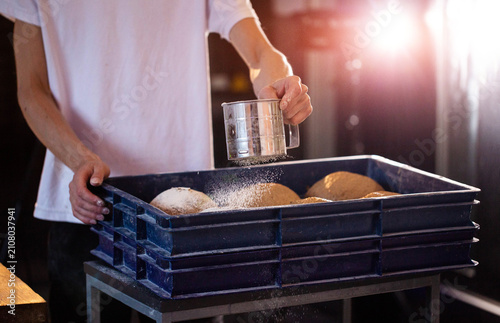 Quadro em tela Baker hands sift flour over bread dough in blue crate manual preparation of arti