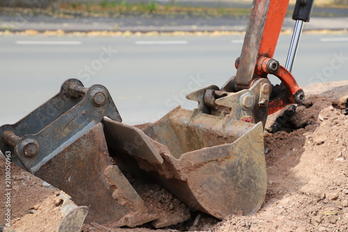 Canvas Print Excavator bucket digging a trench beside a temporary safety barrier during road construction