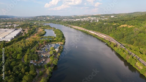 Moselle valley, Mosel river flowing past village, road and railway tracks, lush green hills and cityscape of Trier, landscape in summer, aerial view