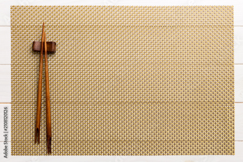 Two chopsticks and bamboo mat on wooden background. Top view, copy space