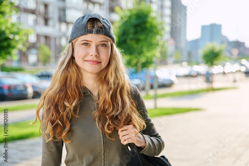 Happy teen girl with backpack and backward cap walking outdoors