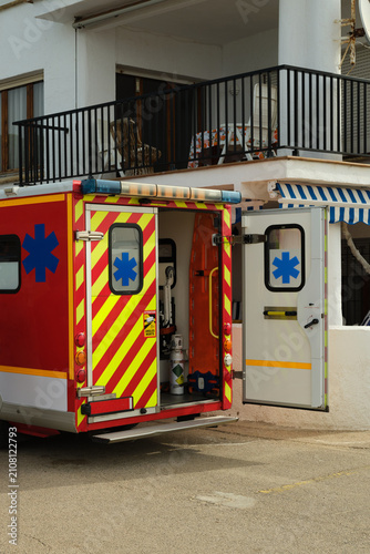 Fotografía Ambulance vehicle with open rear doors showing medical equipment inside, parked near a residential building during an emergency call