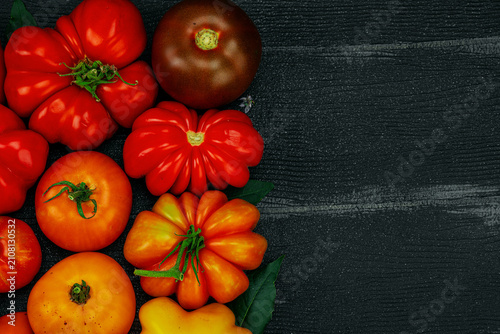 Принти на полотні Assorted homegrown heirloom tomatoes with small flowers on a dark wooden background