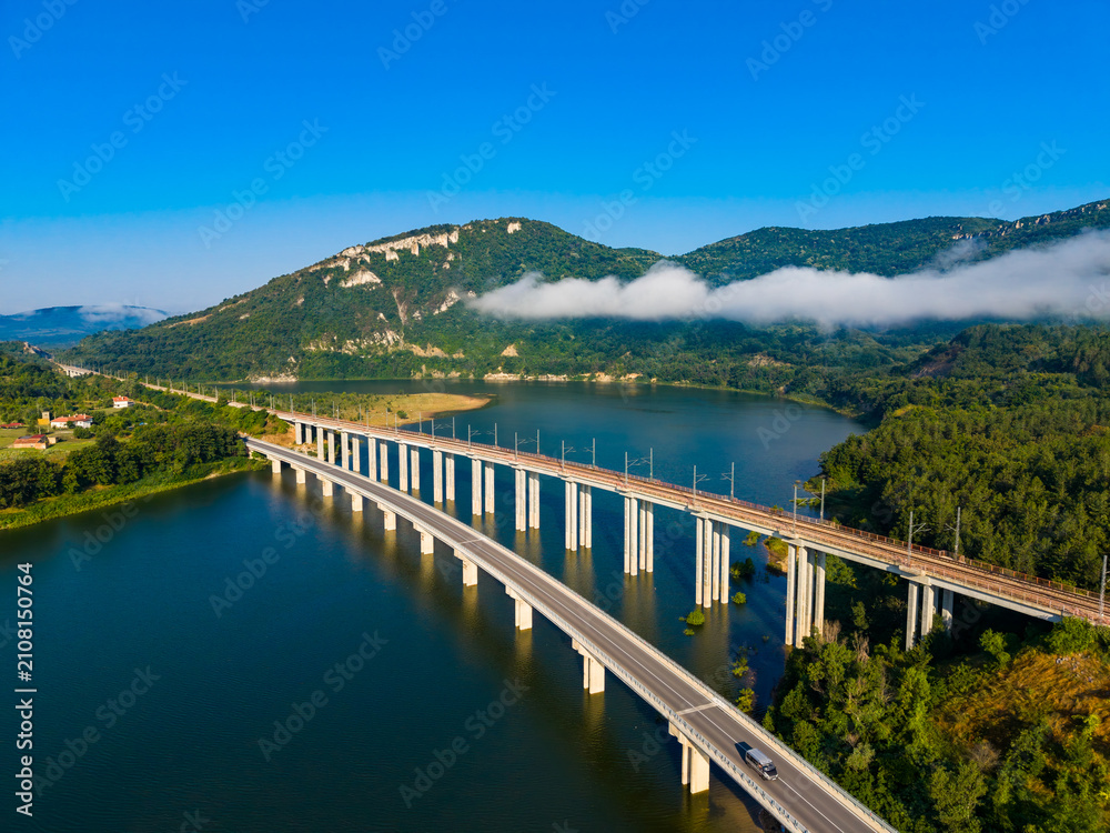 Fototapeta premium View of a bridge over a river with mountains and blue sky in the background in the early morning hours