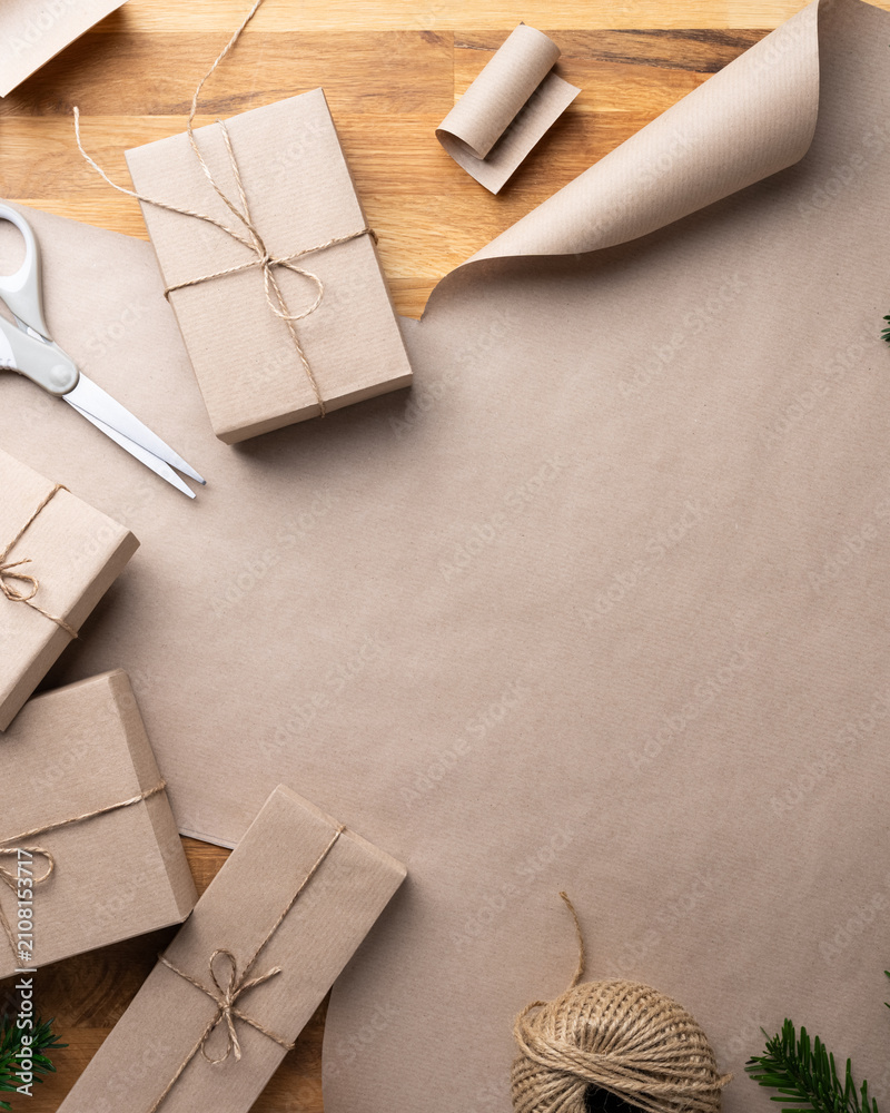 Obraz premium Top view of handmade Christmas gift wrapping with kraft paper, twine and evergreen branches on rustic wooden background with copy space.