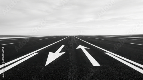 Directional Arrows Mark Asphalt Road Leading Towards Horizon Under Overcast Sky