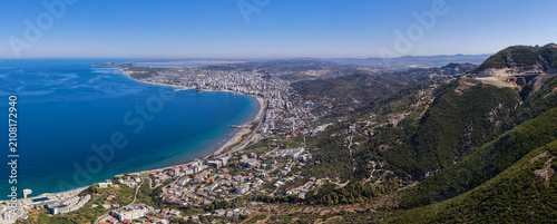 фотографія Sweeping aerial panorama showcasing the beautiful curvature of Vlora Bay, bustling city waterfront, and a prominent mountain road carved into the steep green hillside in Albania