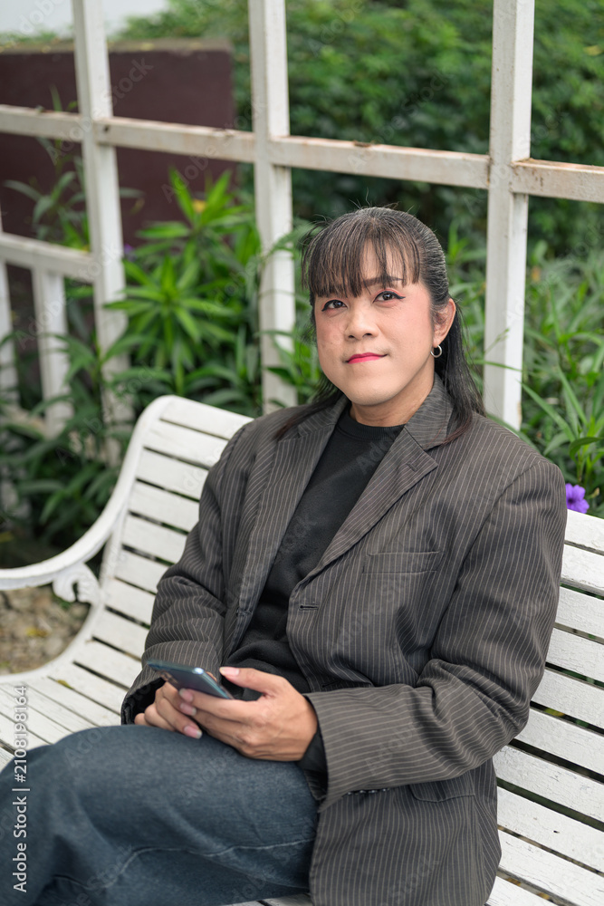 Fototapeta premium Vertical Portrait of Asian Person Sitting on Outdoor Bench Looking at Camera