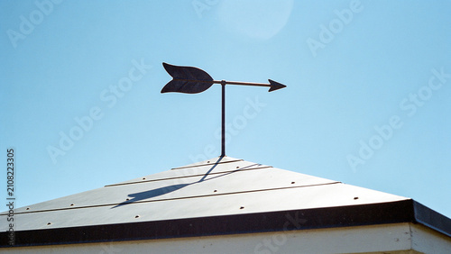 Vintage arrow weather vane on roof pointing direction against clear blue sky