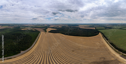 Fotografie Curved field panorama with neat furrows under cloudy sky
