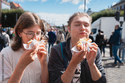 Young Couple Savoring Traditional Hot Dogs Outdoors in Copenhagen