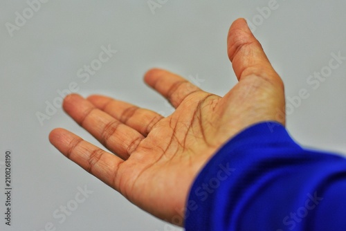 An open human palm with extended fingers wearing a blue long-sleeved shirt against a neutral grey background.