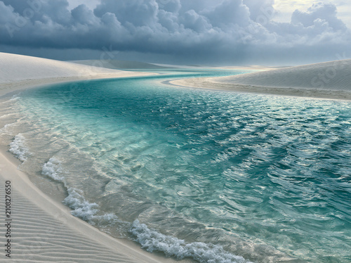 Stunning landscape of lenis maranhenses national park in brazil, featuring white sand dunes and crystal clear turquoise rainwater lagoons under a dramatic cloudy sky