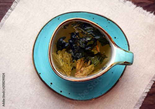 Herbal green tea with dried ginkgo biloba leaves and other dried herbs in a blue ceramic cup on a fringed cloth napkin.