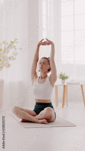 Woman in yoga clothes stretching back and arms on rug at home