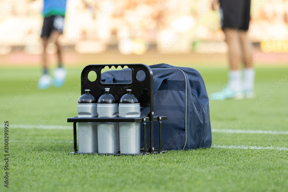 Obraz premium Soccer Hydration. Sport bottles of fresh water or energy drink on a soccer, football field. Players and Balls on Background