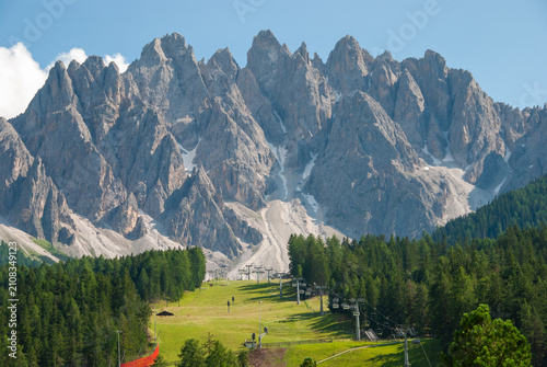 Dramatic Dolomites peaks near San Candido, Italy, with alpine forest, ski lift and green meadow under a clear blue sky. Stunning mountain landscape for travel and nature themes.