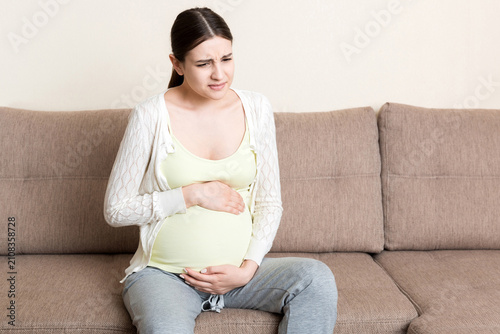 Pregnant woman with painful belly on sofa at home