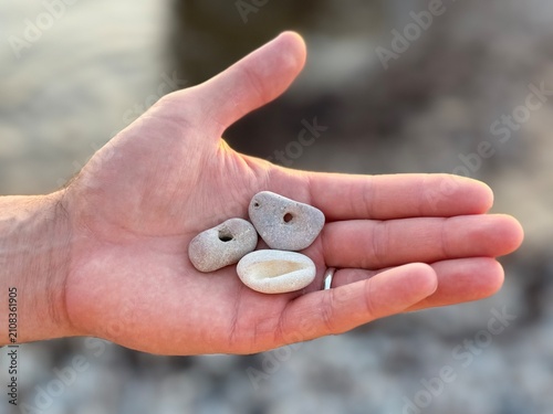 Фотография An open hand holds small, naturally holed stones, often known as hag stones or adder stones