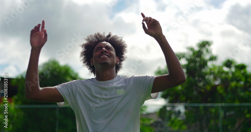 Fotografie Young African American man raising hands toward sky outdoors, expressing joy, fa