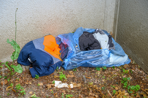 Фотография Discarded clothes and blue plastic bags filled with garments on dirty ground nex