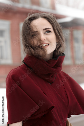 Portrait of a smiling young woman in a burgundy coat outdoors during winter. Natural beauty, lifestyle, fashion and seasonal concept.