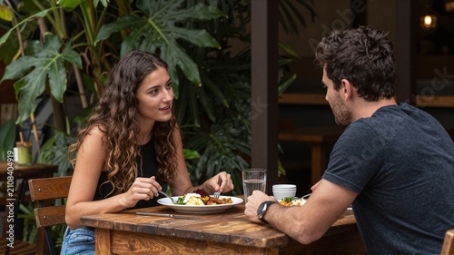 Couple eating dinner at outdoor restaurant with green plants.