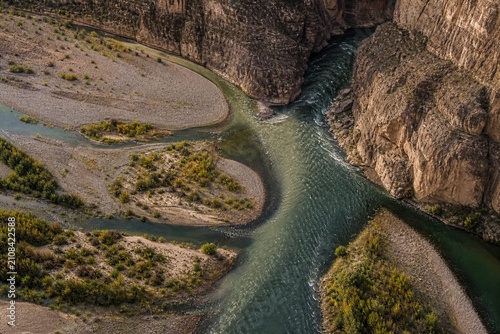 River tributary merging seamlessly with main stream at canyon entrance, aerial view.