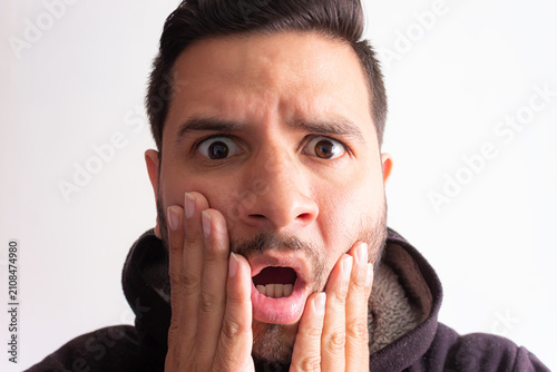 фотографія Portrait of a young Latino man, impressed and with his mouth open, staring at the camera against a white background in a photography studio