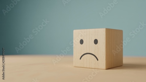 Sad wooden cube block with a hand-drawn unhappy face expression on a neutral background, concept of negative emotions, mental health, and bad mood representation