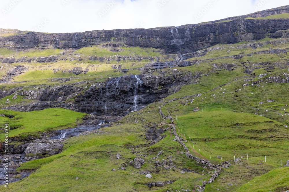 Fototapeta premium Waterfall Cascading Over Rugged Cliffs in Faroe Islands