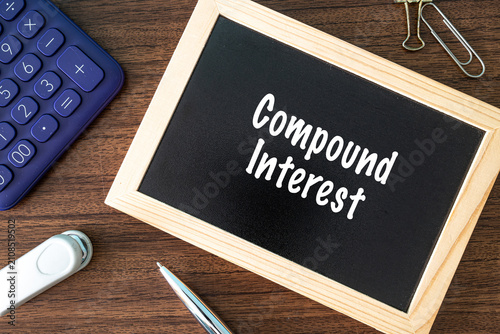 Compound Interest text on black chalkboard with calculator and office supplies on wooden desk, finance and banking concept