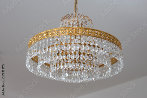 Elegant crystal chandelier with gold frame captured in close-up. Luxurious ceiling light fixture adding sophistication to interior spaces. Detailed close-up of a gold-framed chandelier.