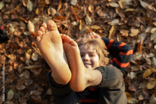 happy little boy lies on ground, which is carpeted with fallen leaves, with his bare feet raised in the air. Childhood happiness, joy, freedom, carefreeness, warm sunny autumn days. selective focus