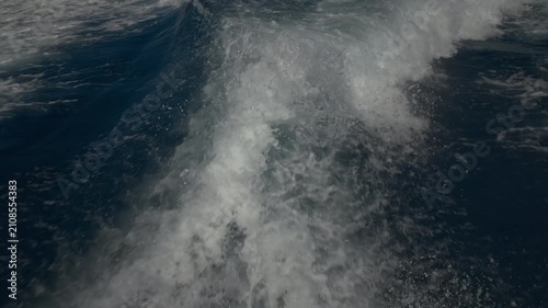 Turbulent white foam water trail behind a large boat in a calm blue sea on a sunny day, slow motion