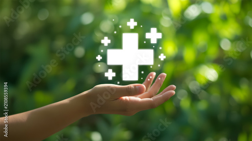 Hand Holding Glowing Medical Cross Icon over Green Bokeh Background - Healthcare, Wellness, and Life Insurance Concept