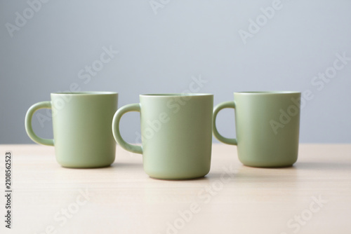 Three matching sage green mugs displayed on light wood surface