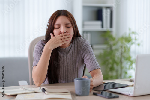 Принти на полотні Young Asian woman yawning at desk while working from home in bright modern livin