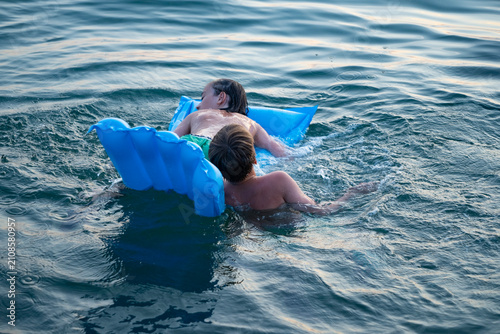 Photography Two children swimming in sea, adrift on blue inflatable raft, accident in open w