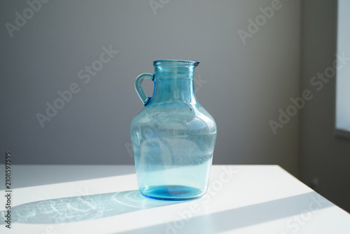 Blue glass jug with handle on white table with sunlight and shadow patterns