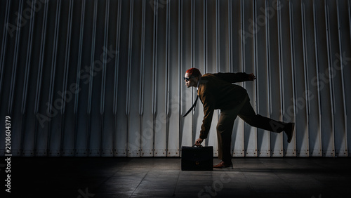 Silhouette of a man in a suit running and picking up a suitcase from the on a dark and dramatic background