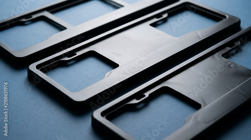 Three Black Automotive License Plate Frames Arranged in a Diagonal Line on a Textured Blue Surface Creating a Sleek and Modern Automotive Accessory Display