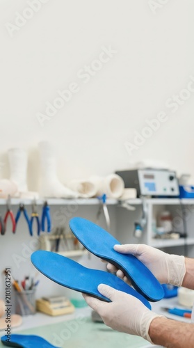 Blue custom orthotic insoles held in laboratory by gloved hands for foot health awareness product display and medical device banner