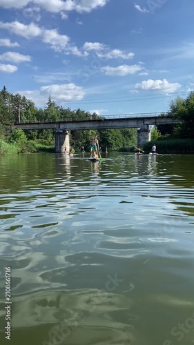 Man paddleboarding with corgi dog on calm water during summer day. Outdoor recreation, companionship, and adventure activity with pet on SUP board. Vertical video.
