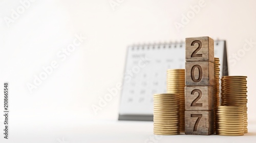 Stacked coins with the year 2027 written on wooden blocks, beside a calendar, signifying financial growth and future planning.