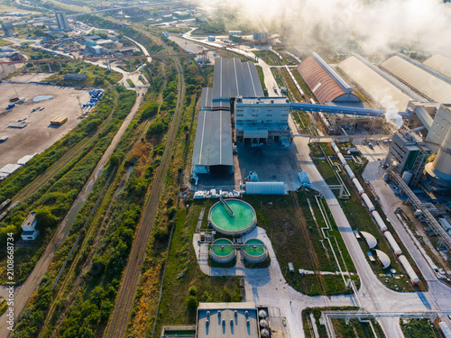 Factory site with large buildings, industrial equipment, and green tanks showing process and activity during daytime hours